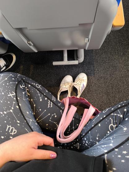 Das Bild zeigt meine Beine im Schneidersitz. Ich trage schwarze Leggings mit einem Sternenmuster. Meine Schuhe stehen vor mir auf dem Boden.