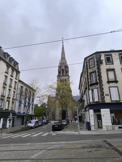 Blick auf die Kirche Saint Michel aus einiger Entfernung. Rechts und links davon Gebäude. Der Himmel ist bewölkt.