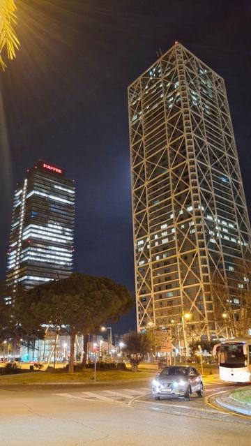 Vista de la Torre Mapfre i l'Hotel Arts de Barcelona des del carrer de Salvador Espriu. La llum dels edificis, del carrer i dels cotxes contrasten amb la foscor del cel nocturn.