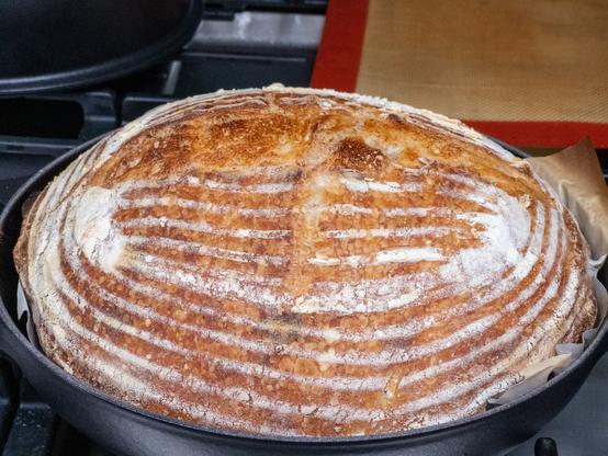 A freshly baked round loaf of bread with a patterned crust in a baking pan.