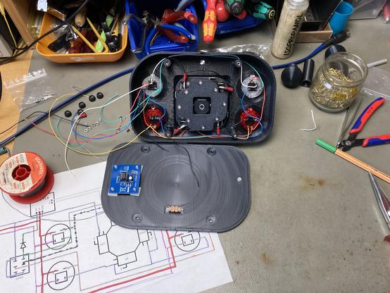 The Open Source Arcade Stick half-way assembled and wired up on my workbench. Wires are hanging out of the enclosure and several tools and a wiring diagram are spread around.