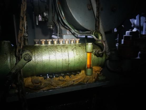 Grüner Zylinder welcher von einer Taschenlampe angeleuchtet wird. Er scheint ölig zu sein.