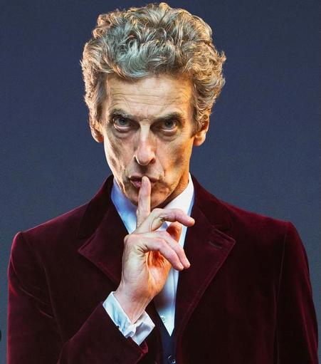 Peter Capaldi as the 12th Doctor. He has his finger to his lips and is saying shhhh..
He is dressed in maroon velvet sports coat with button down blue shirt. No tie.