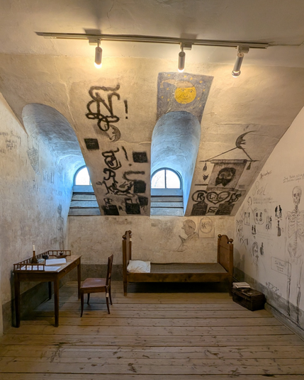 Studentu karceris Tartu universitātes bēniņos. Sienu zīmējumi daļēji atjaunoti pēc ugunsgrēka. Pie sienas galds un krēsls, gulta, kaste ar grāmatām. Vēl telpā ir krāsns, mazgāšanās bļoda un ateja.