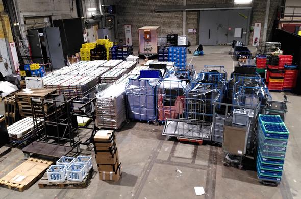 Lagerhalle mit Paletten voll Tischen und Getränkekisten, und diverse Kisten

Logistics hall full of pallets with tables, bottle crates, and various boxes and other things