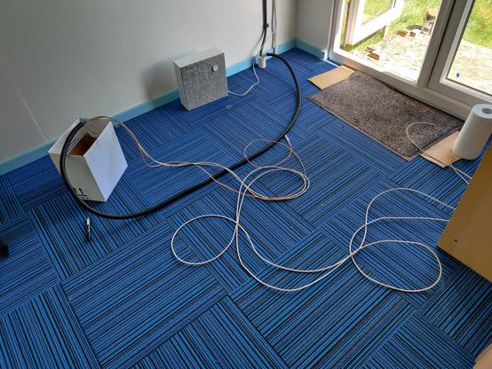 The floor inside RC2014 Towers with black conduit running on it and some grey ethernet cables and an orange fibre cable coming out.