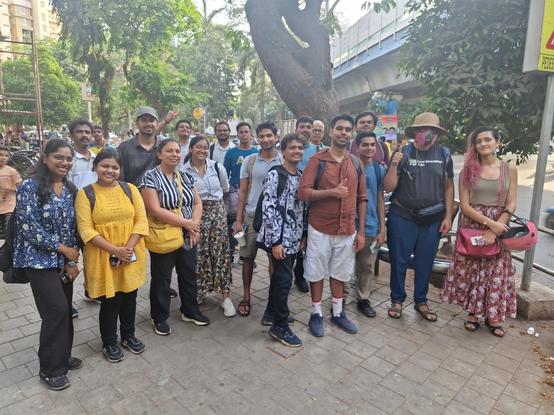 13 men and 5 women standing on the sidewalk near King's Circle, looking at the camera. One is wearing an OpenStreetMap India T-shirt. Two are making thumbs-up signs and another is flashing a V-sign. Photograph by Irfan (Irfus).