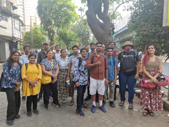 13 men and 5 women standing on the sidewalk near King's Circle, looking at the camera. One is wearing an OpenStreetMap India T-shirt. One is making a thumbs-up sign and another is flashing a V-sign. Photograph by Irfan (Irfus).