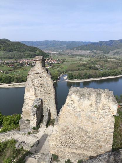 Im Vordergrund Gemäuer einer Ruine. Dahinter im Tal ein großer Fluss und dahinter zwei Ortschaften in der Ferne.