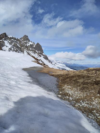 Foto. Berglandschaft mit einem gefrorenen Schmelzwassertümpel am Übergang von Schnee zu aperem Grat.
