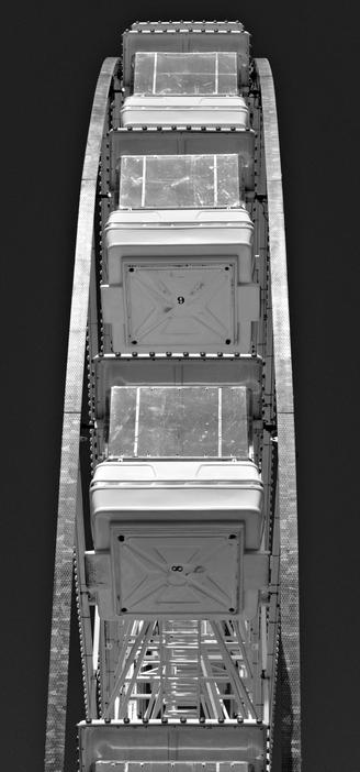 A black and white photograph of a Ferris wheel. Taken end on in portrait format and pointing my camera and lens near straight up. The main focal point is Pods 8 and 9.