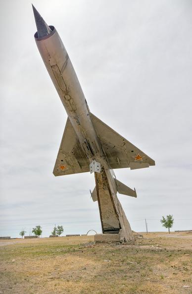 A Soviet MiG raised up on a concrete plinth. The picture is taken from underneath and the Mongolian grass steppe can be seen beyond