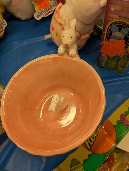 A ceramic bowl with a small white rabbit at the bottom staring up at a much larger white rabbit at the rim.