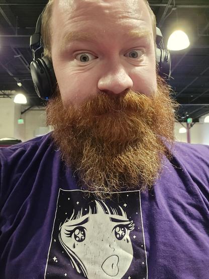 Selfie of a balding, bearded white man wearing black headphones and a purple shirt with a white anime inspired character at the center with starry eyes.