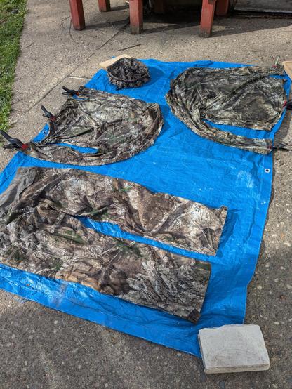 Camouflaged clothing is clipped to a blue tarp laying on a concrete patio outside. The clothes have been sprayed with permethrin, a substance which will repel ticks and other insects, but especially ticks. I hate ticks. I'd burn them with fire, but permethrin will do just nicely.