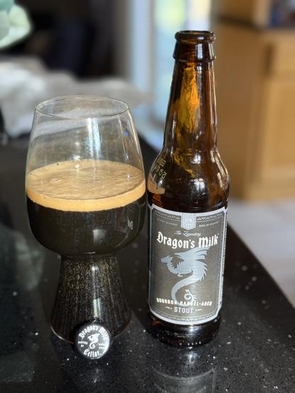 A stout glass of dark beer. The brown bottle has a black and silver label with a dragon in silhouette