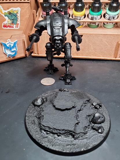 Photo of an assembled Knight Armiger Helverin and a custom base both primed sitting in front of paint storage on a desk.