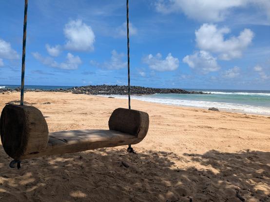 A wooden swing in the foreground and an empty Hawaiian beach behind.