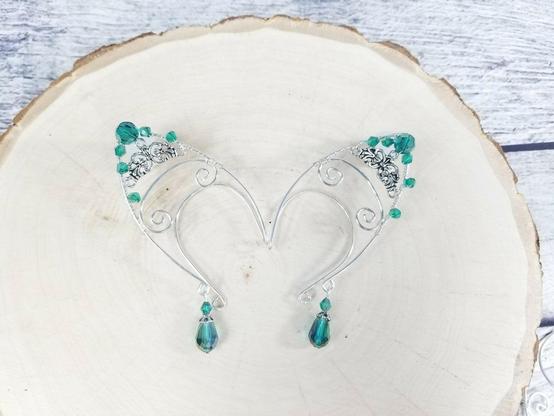 A pare of silver filigree ear cuffs with turquoise beads sit on a wooden pedestal.