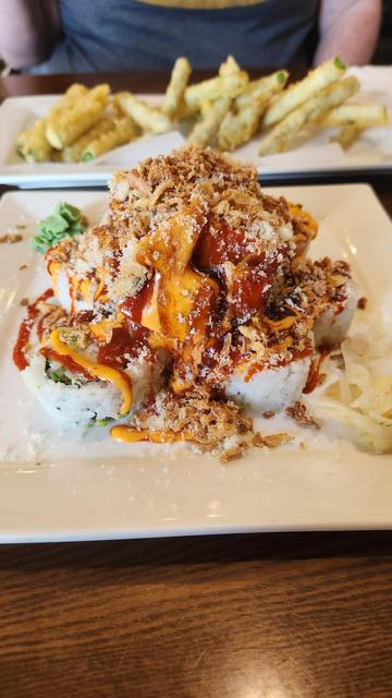 A california roll on a plate that is PILED with tuna sashimi and covered with tempura crisps and sauces. In the background is a plate with asparagus tempura.
