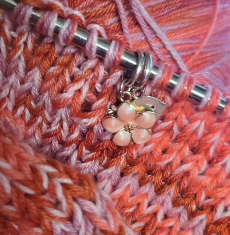 Close up of pink enamel cherry blossom stitch marker on pink-coral marled stockinette stitch