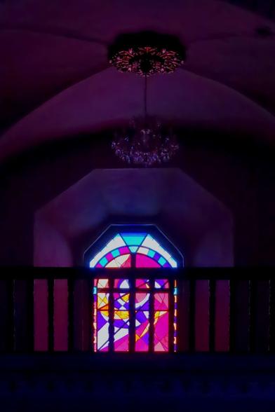 Inside a church, a window with a stained glass in purple pink colours