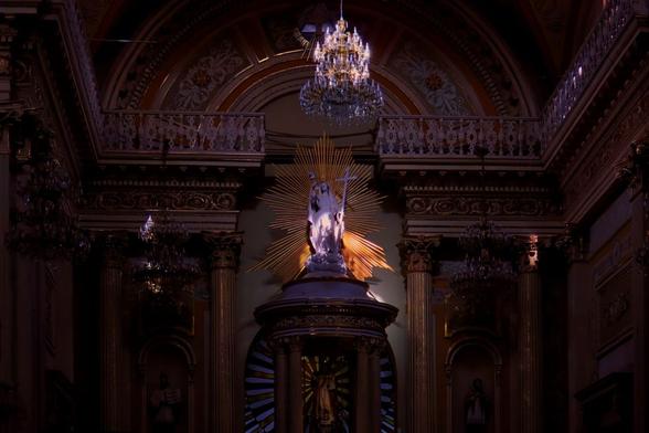 A sculpture of the virgin, in a situation where the light is hitting the sculpture and the rest of the church is Dark