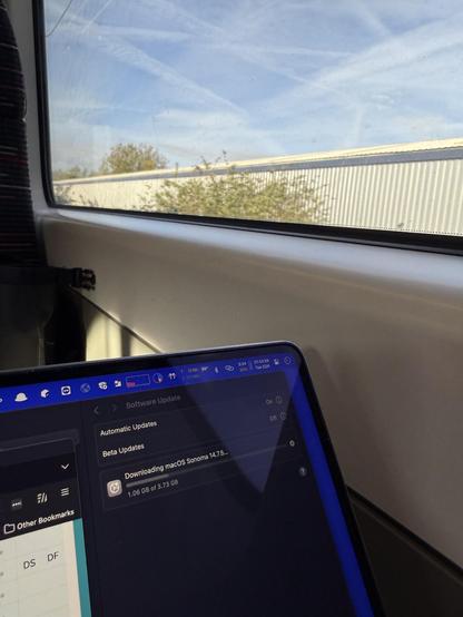 a photo of the corner of my laptop screen showing that I’m downloading a 3GB macOS update while tethering off my phone. i’m in a train and you can see the sky through the window in the background