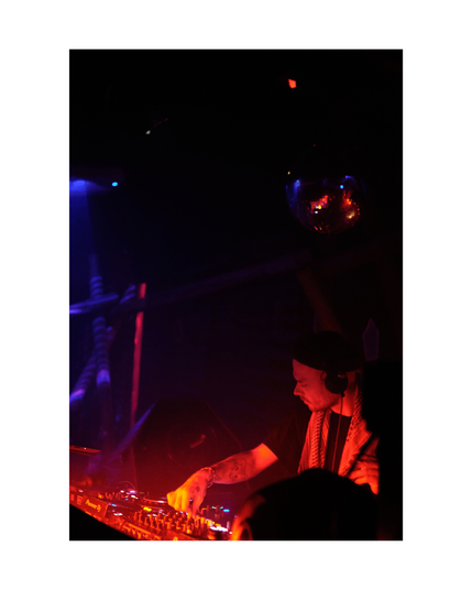 young man looking down, focused on djing, in low key club situation with red lighting