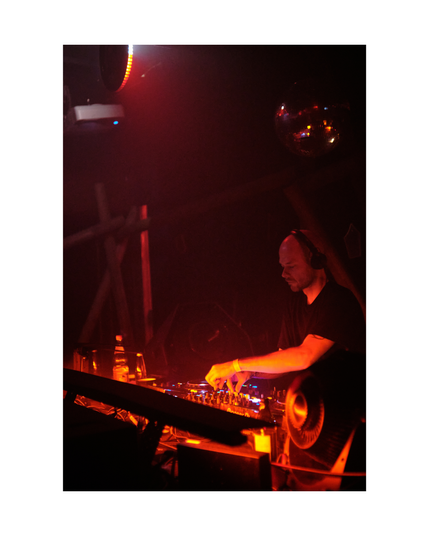 young man looking down, focused on djing, in low key club situation with red lighting