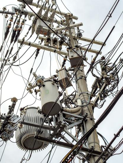 Local electrical utility pole showing mass of wires and oil filled transformers.  High contrast.