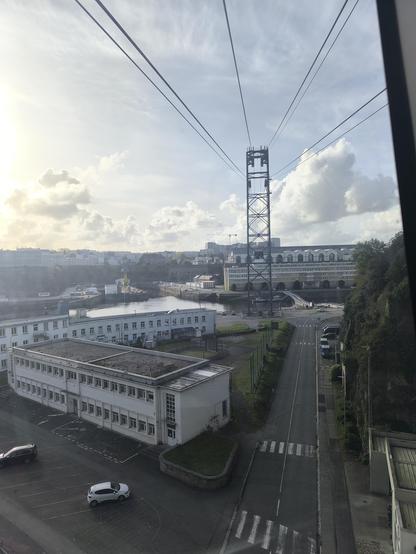 Blick aus der Seilbahn-Kabine. Unten I'm Bild sind Gebäude, in der Mitte ist der Fluss und ein Teil vom Hafen zu sehen. Darüber ein teilweise bewölkter Himmel.
