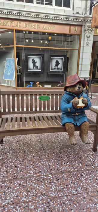 Statue of Paddington bear eating a sandwich.