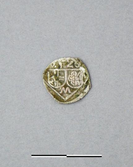 Photo: M. Simon/ Novetus

The image shows a silver coin from the 16th century, exhibiting significant wear and discoloration. The coin's surface is tarnished, suggesting age and exposure to the elements. The design features a central shield with heraldic symbols, indicating a specific noble family or jurisdiction. An "M" is visible within or below the shield. The numerals visible above the represent a date.