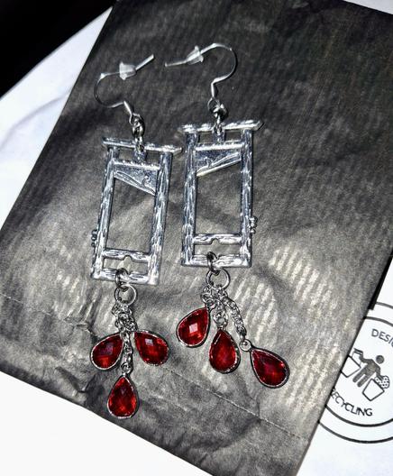 A pair of long drop sliver toned earrings shaped like mini guillotines, with little chains at the bottom of each earring, with three red blood-drop shaped crystals at the bottom of each chain. They are fabulous. They are also unfortunately photogrpahed on a black paper bag which makes this a difficult phot, my apologies for that.