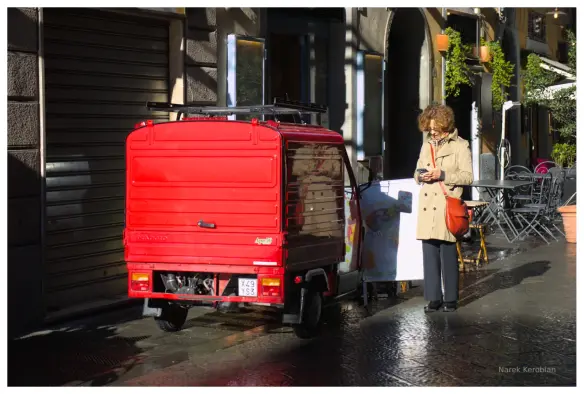 A woman with red purse standing next to a red moped truck