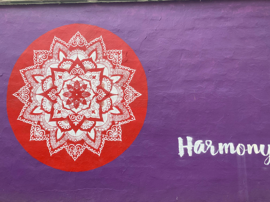 Color image of a Mandala noting Harmony along a public walkway in Indianapolis, Indiana, USA. Image shows a red mandala printed on a purple background, with the single word "Harmony" in the field of purple, in a public installation by Jamie Locke Art. and Megan Jefferson, sponsored by the Indianapolis Department of Public Works.