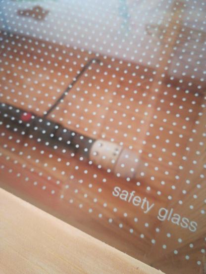 nærbillede af køleskabspladen. den er af glas og der er trykt teksten "safety glass" på glasset samt små hvide prikker (som tilfældigvis passer ret godt på størrelserne af ternene på ternet papir).