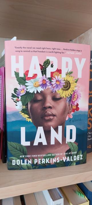 Book cover of Happy Land with photo of black woman with flowers in her hair, with a backdrop of blue Appalachian mountains.