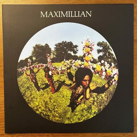 Maximillian front cover, featuring a round, fish-eye lens view of the three band members, wearing very colorful regalia and positioned on crucifixes covered in flowers.