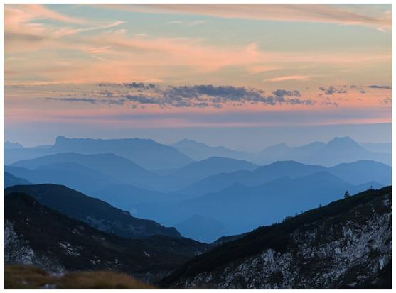 Layered blue mountain ranges fade into a soft, pastel-streaked sky at dawn.