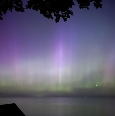 A view of the Northern Lights over water. Mostly colored green, with a few vertical beams of purple light.