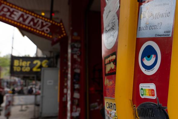 Our Nutriscore BAZED sticker, imitating the design of typical nutriscore labels, stuck to the entrance of the Reeperbahn Penny. A big arrow with the name PENNY pointing towards the entrance is visible in the background.