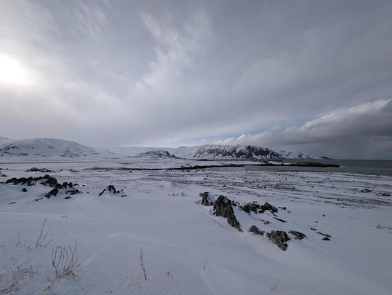 Snowy coastline and mountains, with a calm sea on the right. Cloudy sky.