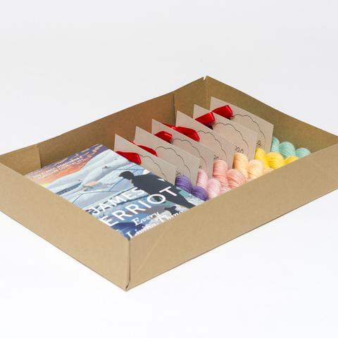 Picture shows an open A4 box containing a copy of James Herriot's 'Every Living Thing' and six mini skeins of yarn in a variety of colours.
