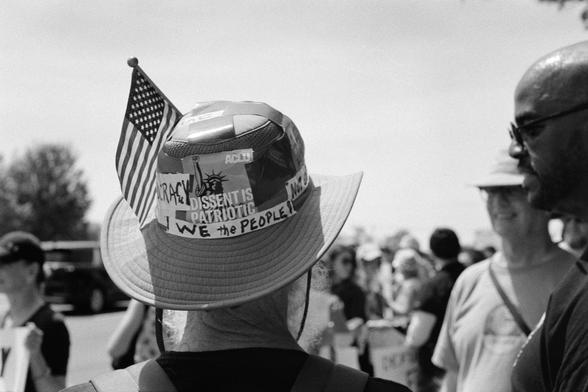 The back side of a protestors brimmed hat covered in stickers and slogans