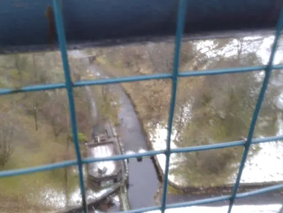 An image of the land below from on top of the dam, wiring can be seen to stop people from falling