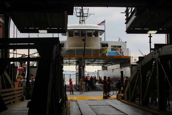People dressed sheik and flappers all around gathered to board the ferry leading to the Governor’s Island in NY, NY for a Jazz Lawn Festival. A person at the dock waves to another on the ferry.