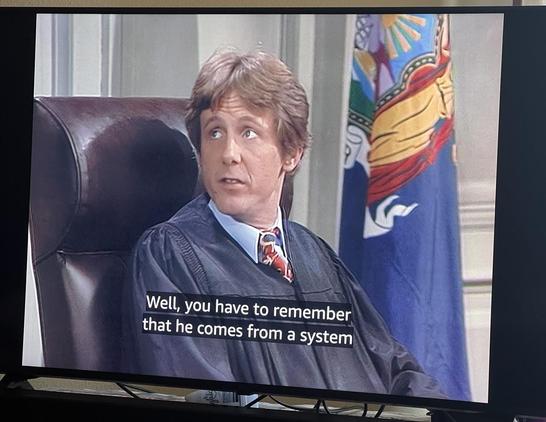 Harry Stone in judge robes, saying “Well, you have to remember he comes from a system”