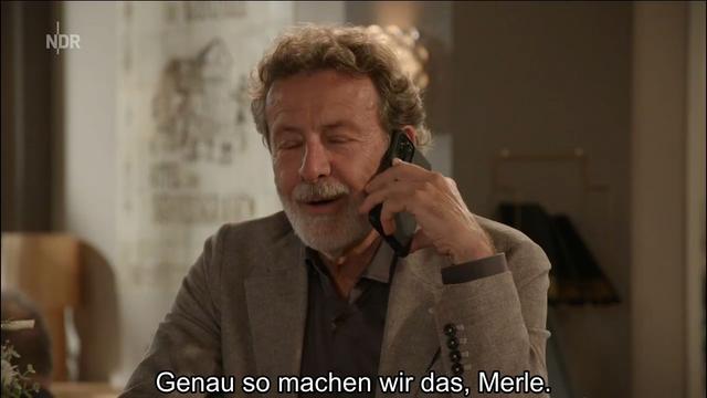 Description: The image shows a man sitting at a table, talking on a cell phone. He is surrounded by a wall, a lamp, and other objects. At the bottom of the image, there is text.

Disclaimer: This image description was automatically generated and may not be entirely accurate.